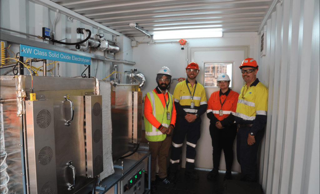 industrial workers stand in front of electrolysis equipment