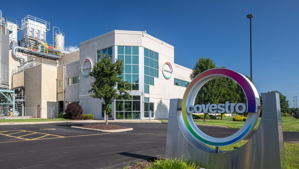 covestro manufacturing site with blue sky behind a white building and brightly colored covestro logo in the foreground